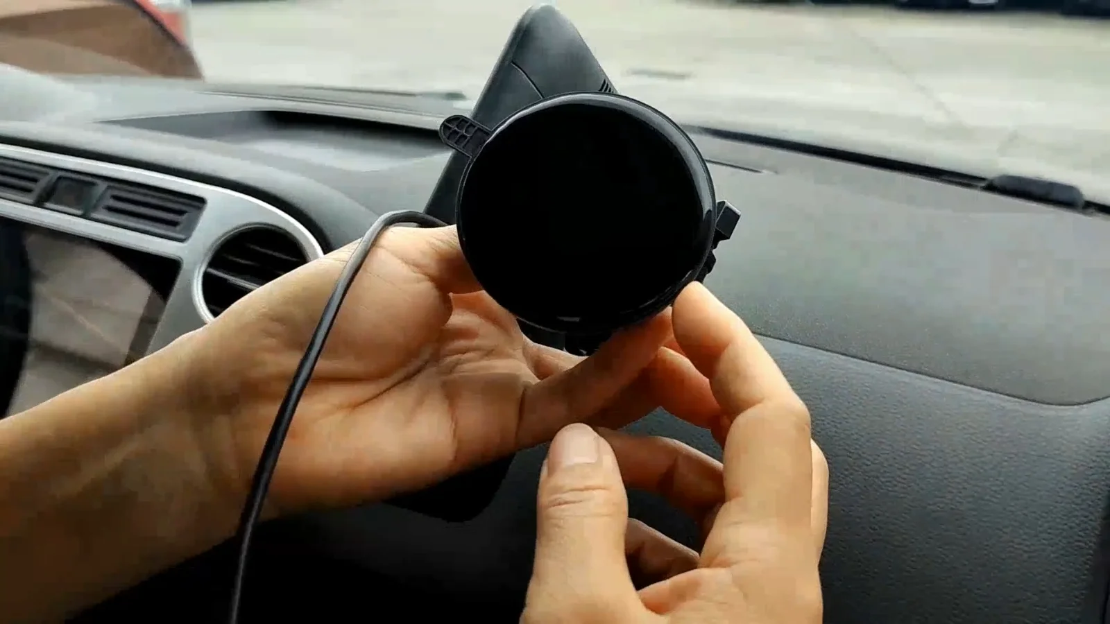 A monitor and its lead held in one hand in a car cabin